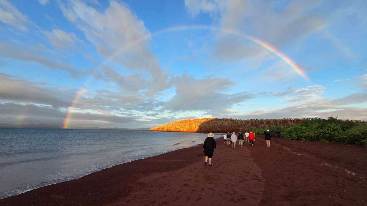 Small group Galapagos tour with Cultured Travel walking Rabida Island's red sand beach under a double rainbow